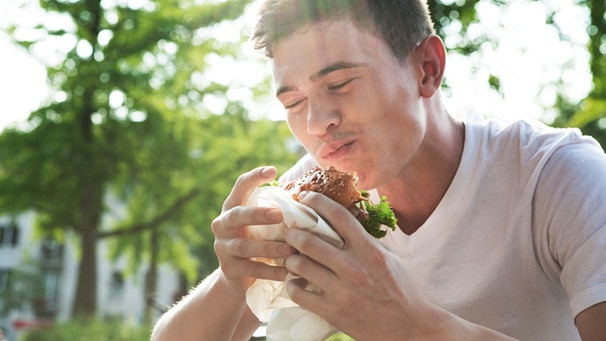Mann isst einen Burger und lächelt | Bild: mauritius images