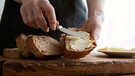 Frau streicht Butter auf ein Stück Brot | Bild: mauritius images / Vladislav Nosick / Alamy / Alamy Stock Photos