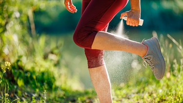 Frau sprüht sich die Beine mit Mückenspray an. | Bild: mauritius images Zbynek Pospisil